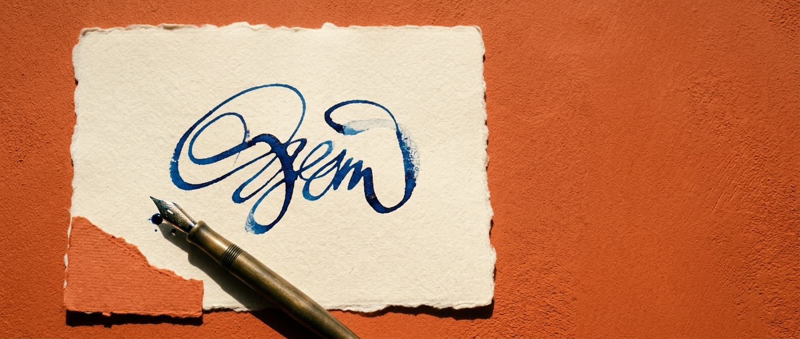 Una firma azul tinta recién hecha se seca sobre una hoja color crema de bordes irregulares, con el plumín de una pluma estilográfica apoyado al lado.